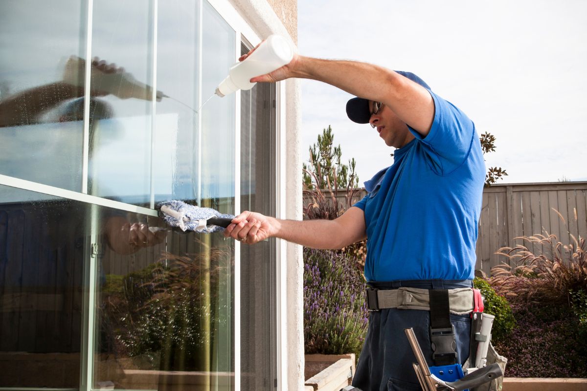 A man wearing a blue shirt and blue jeans is diligently cleaning a window with a cloth.